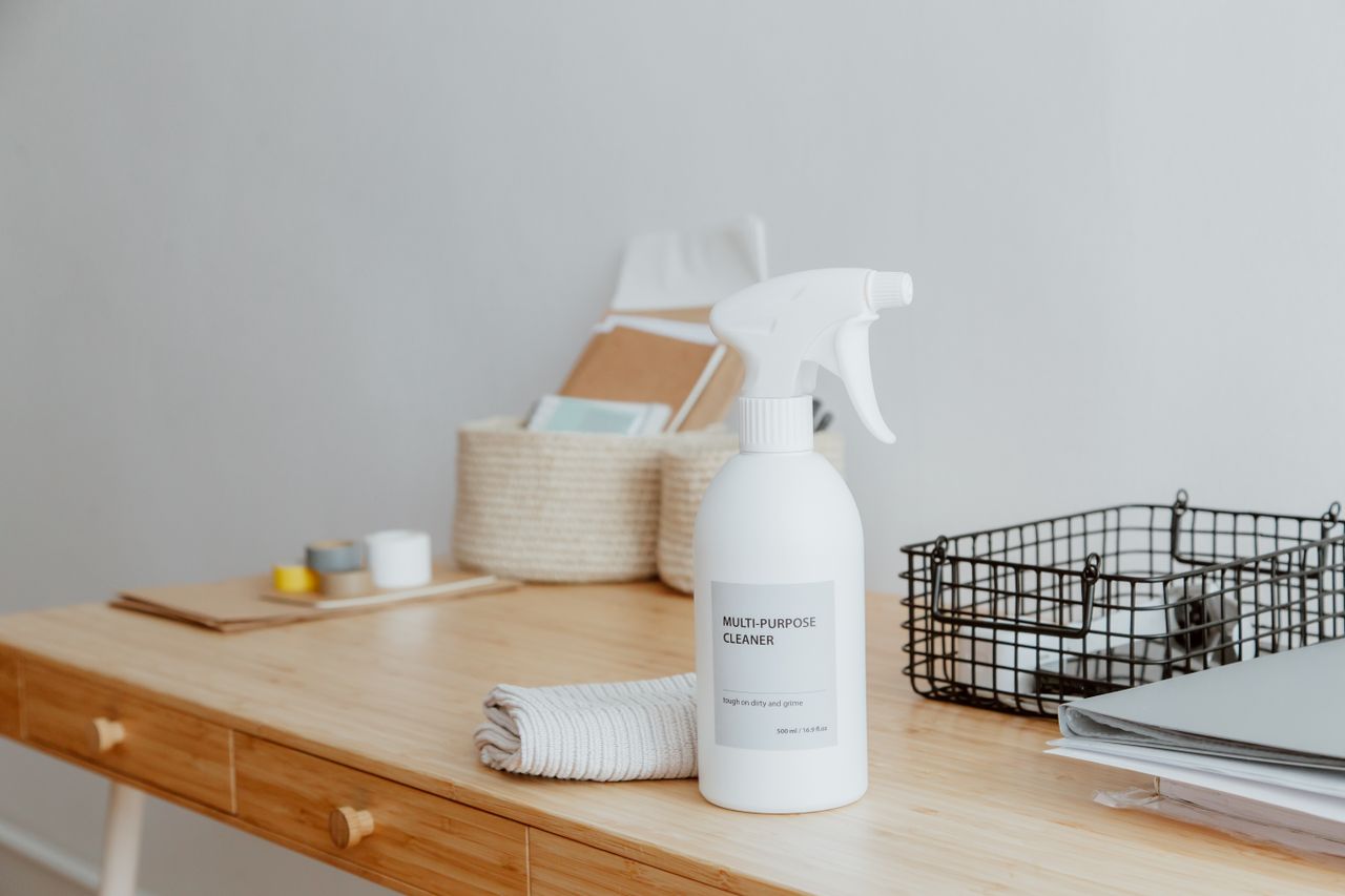 A minimalist desk centered on a multipurpose cleaner, office supplies, and storage solutions.