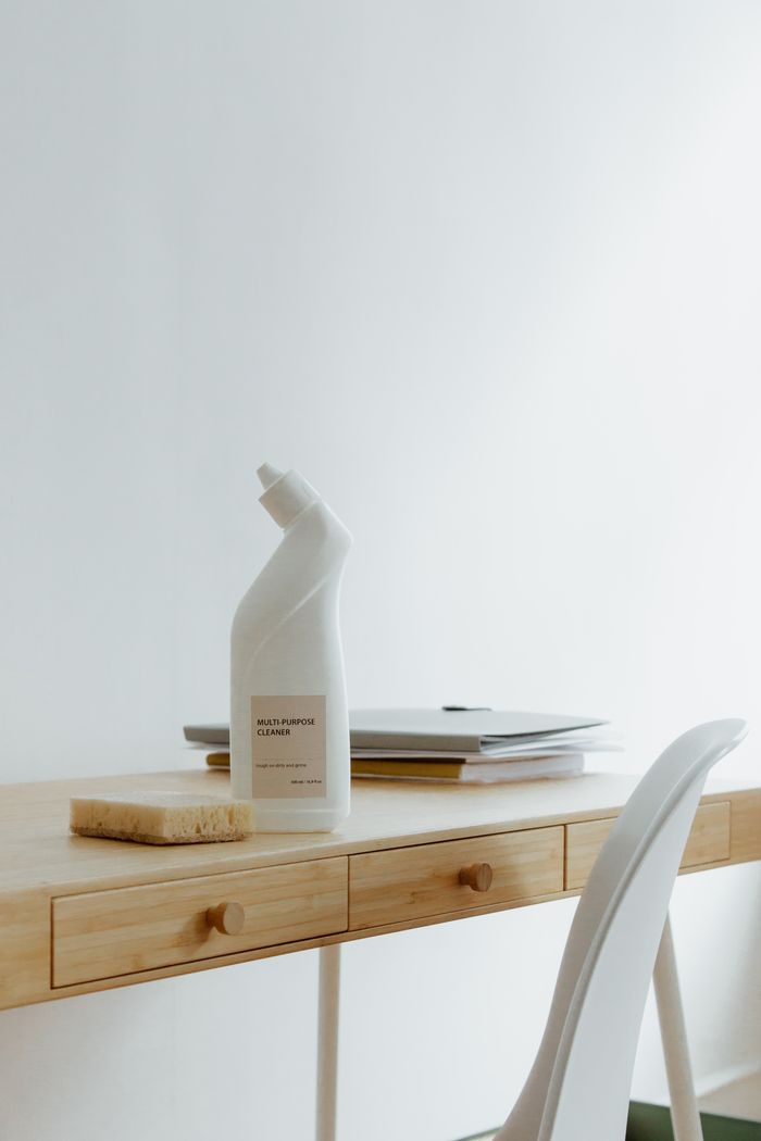A tidy, well-arranged home office desk with a cleaning bottle and sponge, highlighting simplicity and practicality.